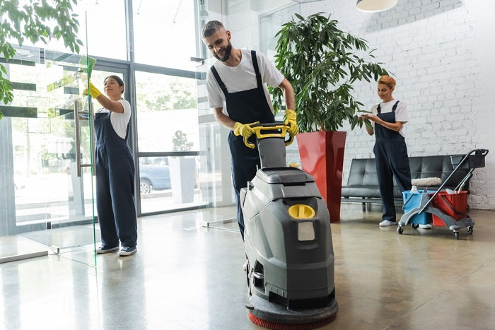 A worker using a floor scrubber machine in a building entry way. 